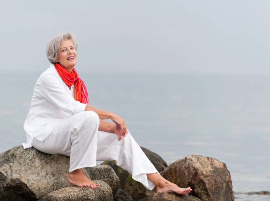 Symbolbild Frau am Strand sitzend auf Felsen. Monatsthema „Gesund alt werden: einfachSchritte“ für ViewMed|Depositphotos @PicterArt|Lizenznehmer: Pressebüro LAAKS